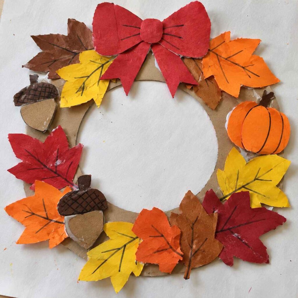 21 Easy & Creative Fall Crafts for Kids to Make at Home 14 Easy Paper Fall Wreath Craft for Kids Make a colorful fall wreath using construction paper and a cardboard ring. Bright autumn leaves, little acorns, a paper pumpkin, and a red bow give this simple craft a cozy Thanksgiving look. Materials Needed: - Cardboard from an old box - Red, orange, yellow, and brown construction paper - Glue stick - Child-safe scissors - Black marker How to Make It: 1. Cut a large ring from cardboard to make the wreath base. 2. Cut simple leaf shapes from fall-colored paper and draw veins with a marker. 3. Make two small paper acorns and an orange paper pumpkin. 4. Glue the leaves around the cardboard ring, overlapping them slightly. 5. Add the acorns and pumpkin, then finish with a simple red paper bow at the top. Quick Tip: Don’t worry about perfectly cut leaves. Slightly uneven shapes make the wreath look more like a real handmade kids’ craft.