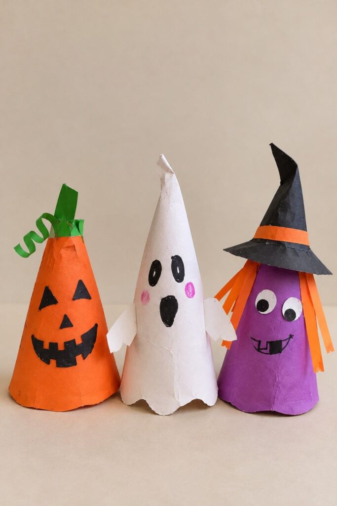 21 Easy & Creative Fall Crafts for Kids to Make at Home 18 16. Easy Paper Cone Halloween Characters for Kids
Turn colorful construction paper into cute little Halloween characters! Kids can make a smiling pumpkin, a silly ghost, and a funny witch using simple paper cones. This is an easy fall craft for Halloween decorating at home or school.
Materials Needed:
- Orange, white, purple, black, and green construction paper
- Pink paper scraps
- Glue stick
- Child-safe scissors
- Black marker
How to Make It:
1. Roll a sheet of construction paper into a cone shape and glue the edge to hold it in place.
2. Trim the bottom so the cone can stand. Make an orange pumpkin, a white ghost, and a purple witch.
3. Add simple faces using black paper or a marker. Give the ghost little paper arms and the pumpkin a green curly stem.
4. Make a small black witch hat with an orange band and glue it onto the purple cone.
Quick Tip: Let kids create their own funny faces and mix up the colors to make every character different.